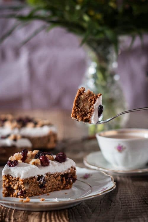Kuchen mit weißer Glasur, Walnüssen und Cranberries auf einem Holzuntergrund und Kaffeegedeck