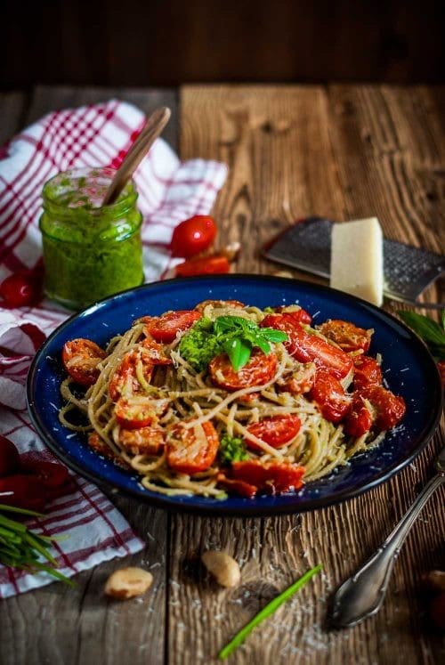 Ein Teller voll Spaghetti mit Tomaten und grünem Pesto auf einer Holzplatte