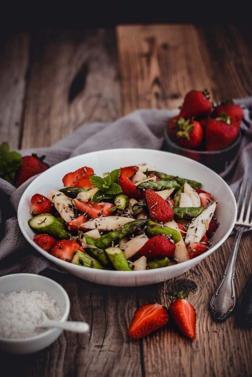 Salat mit Erdbeeren und Spargel auf einem weißen Teller mit Dekoration